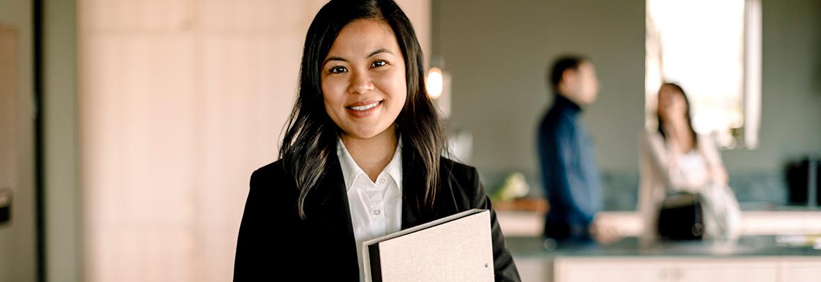 Photo of an asian, female real estate agent with clients in the background