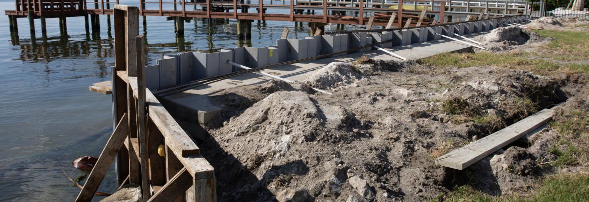 Seawall breakwall construction strengthening work on large body of water - stock photo Seawall break wall concrete strengthening work construction site utilizing wood framing on large body of water with docks, boats and houses in the background on sunny.