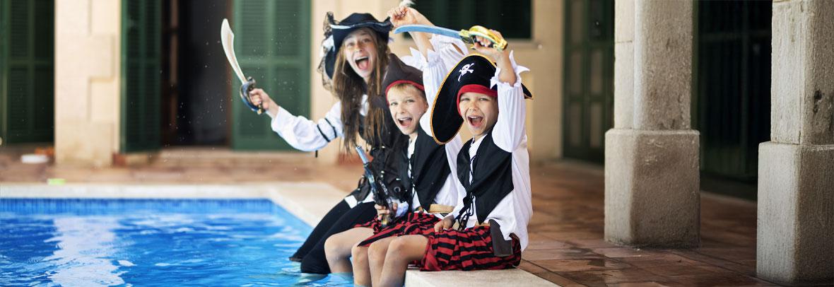 Three kids dresses as pirates dip their feet in a swimming pool