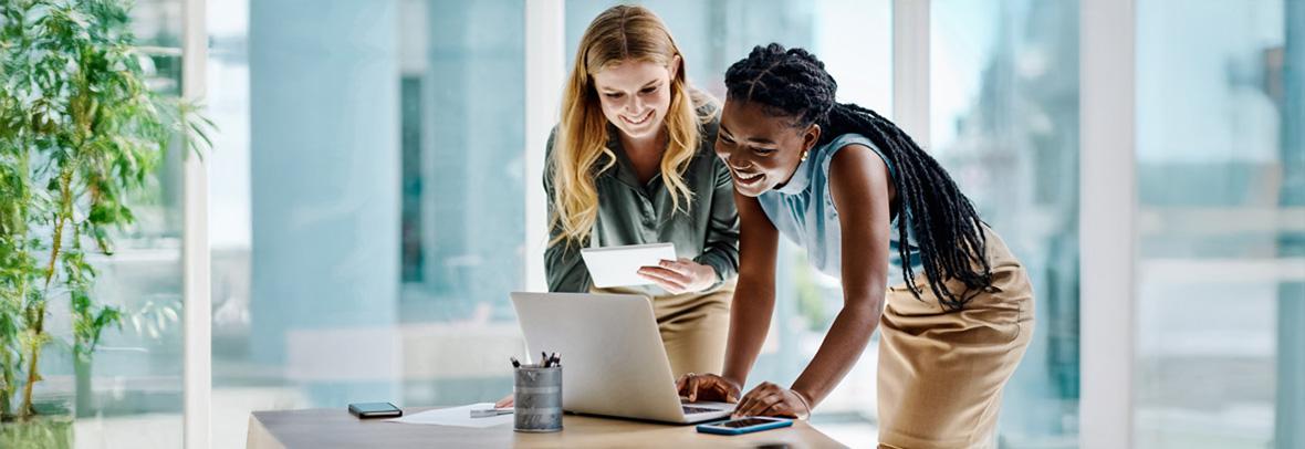 Two businesswomen working together on a digital tablet and laptop in an office