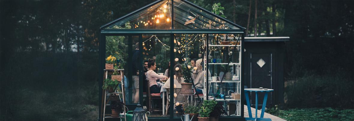 Young multi-ethnic friends enjoying dinner party in glass conservatory room at back yard