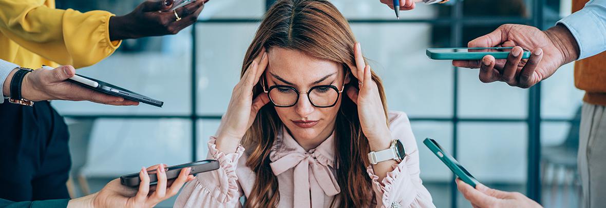 Photo of a stressed woman with hands holding many types of tech out to her
