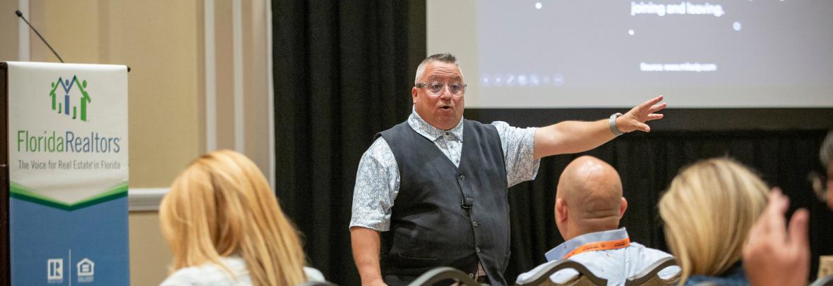 Man with arm extended speaking to a room of people