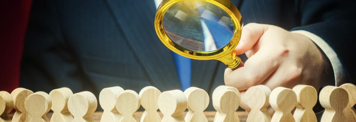 hand holding a magnifying glass over a group of wooden block people