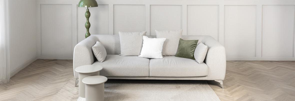 Stylish neutral living room scene featuring a soft beige sofa white cushions, a green floor lamp, and a textured light rug on warm wooden flooring. Demonstrating Pantone color of the year 2026 - Cloud Dancer