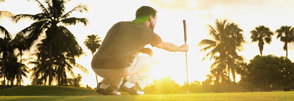 photo of golfer looking at putt with sunset behind him