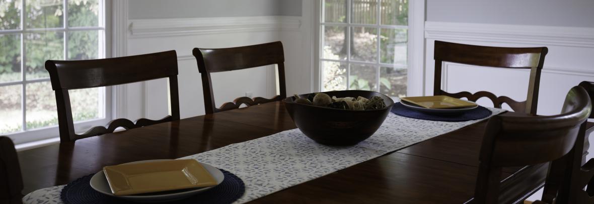A cozy dining area features a wooden dining table paired with matching chairs, set against the backdrop of a serene window framing the lush outdoor view.