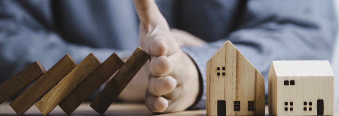 Businessman hand protect and stop wooden house from domino falling wooden bar for risk management and analysis of real estate concep