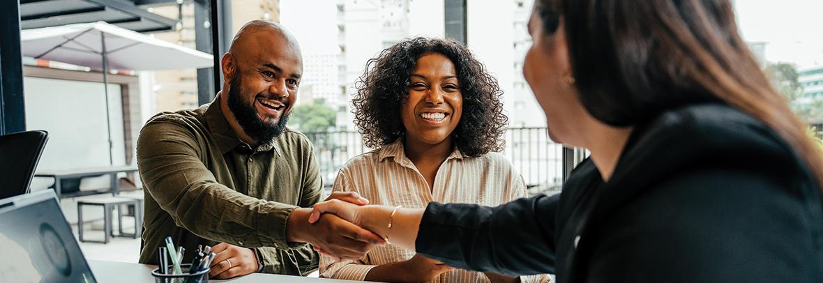 Photo of a real estate agent shaking hands with a couple clients in the office