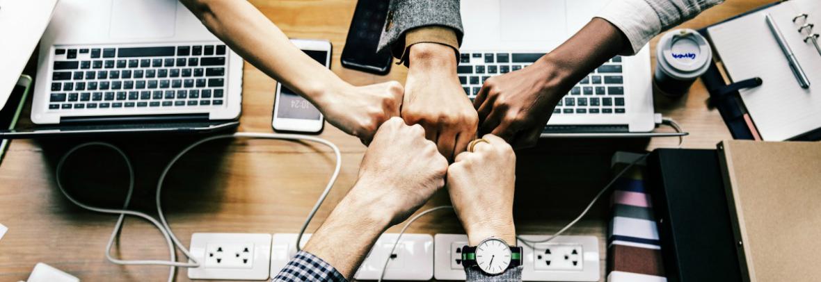 Team of people fist bumps over computers and coffee.