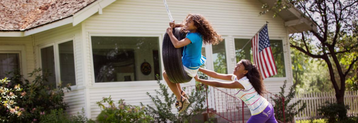 Kids playing on tire swing in front yard of house