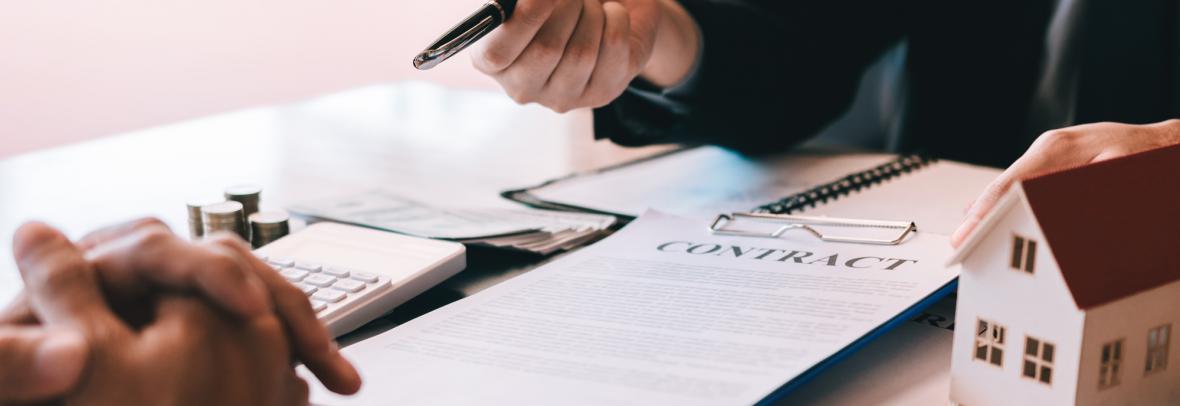 miniature house with house key sitting on top of contract paperwork with hands signing