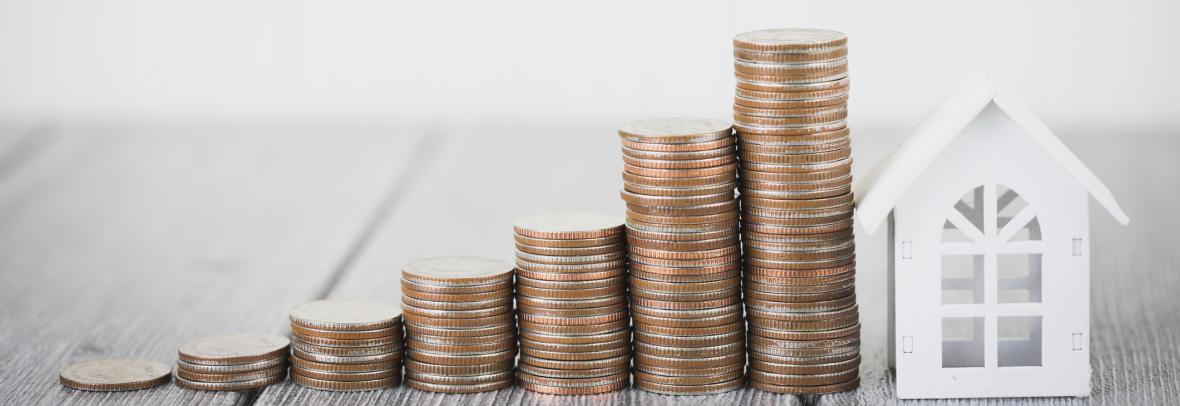 Pequeña casa de papel con monedas apiladas a su lado