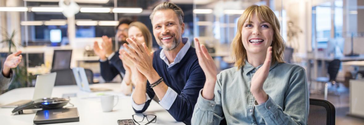 People at an office table clapping and smiling