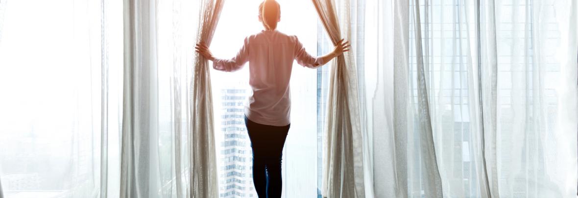 woman holding curtains open looking out window