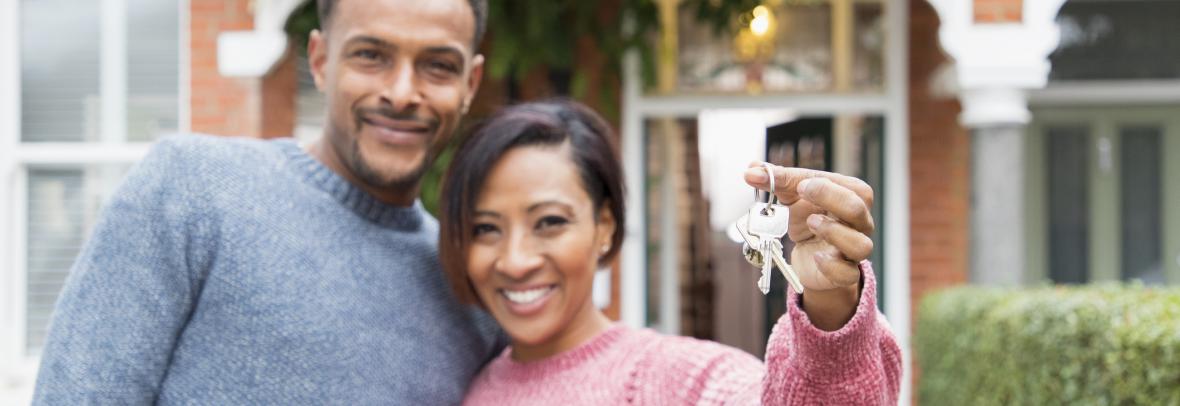 Portrait happy couple with house keys outside new house