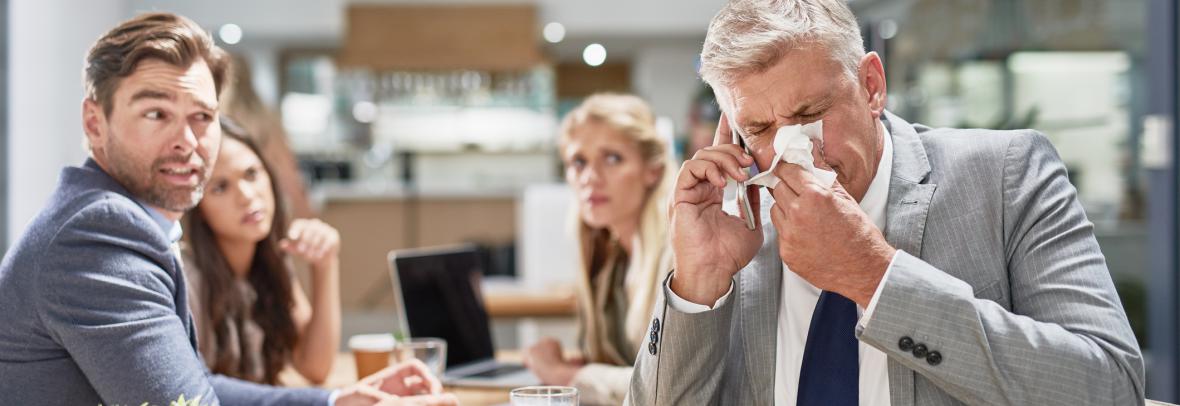 businessman blowing his nose while his colleagues look on in disgust