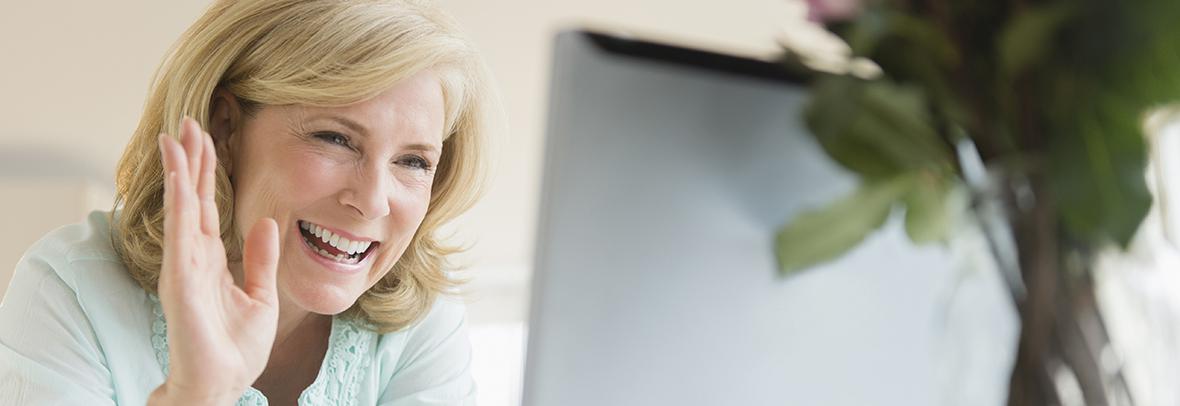 woman smiling and waving at computer screen