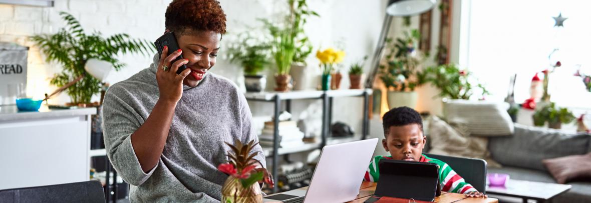 woman on phone and laptop at home with young child