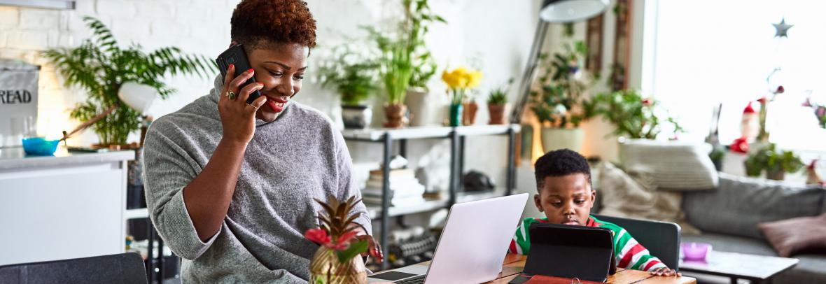 woman on phone and laptop at home with young child