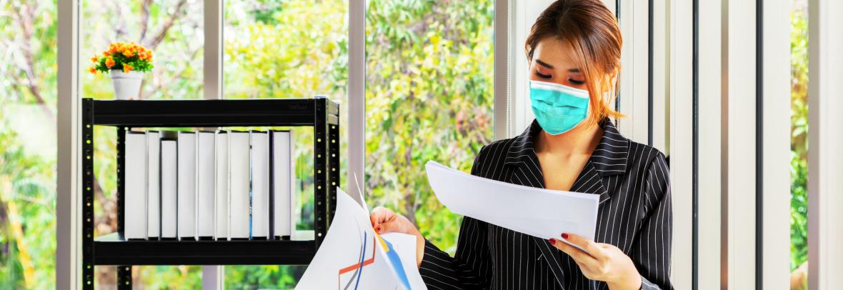 Woman wearing mask in office looking at paperwork