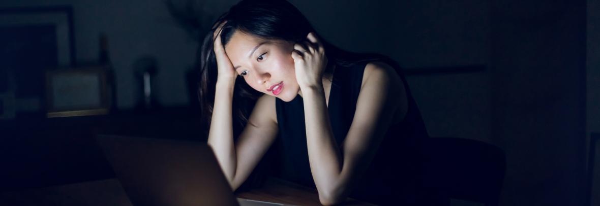 woman in dark on phone looking at laptop