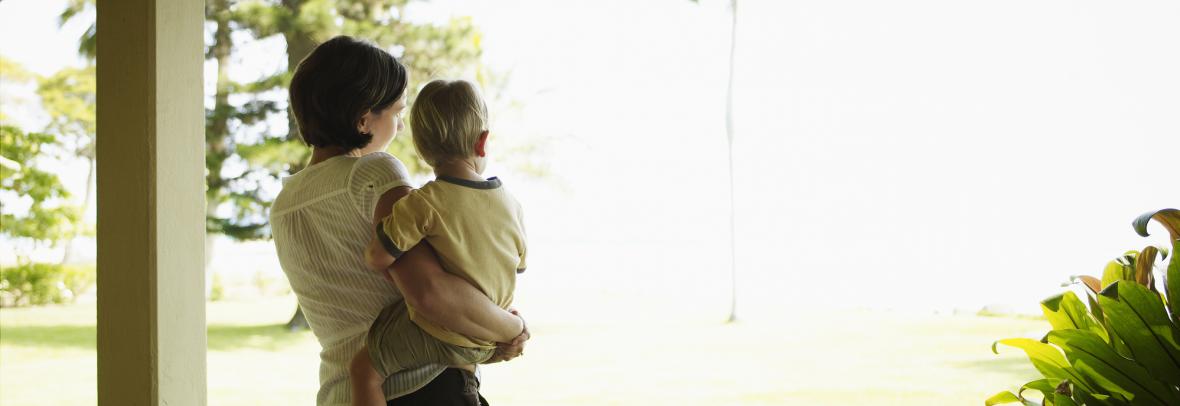 Mother holding toddler son on porch looking out