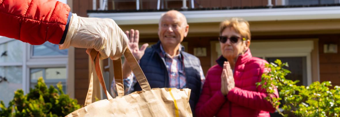 Gloved hand holding grocery bag delivered to thankful older couple 