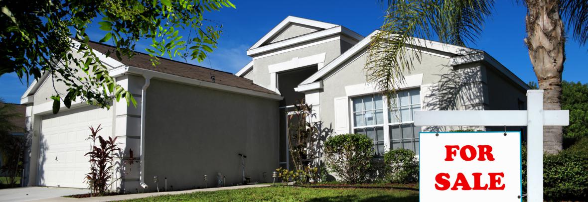 Moderate Florida home with palms trees and a for sale sign