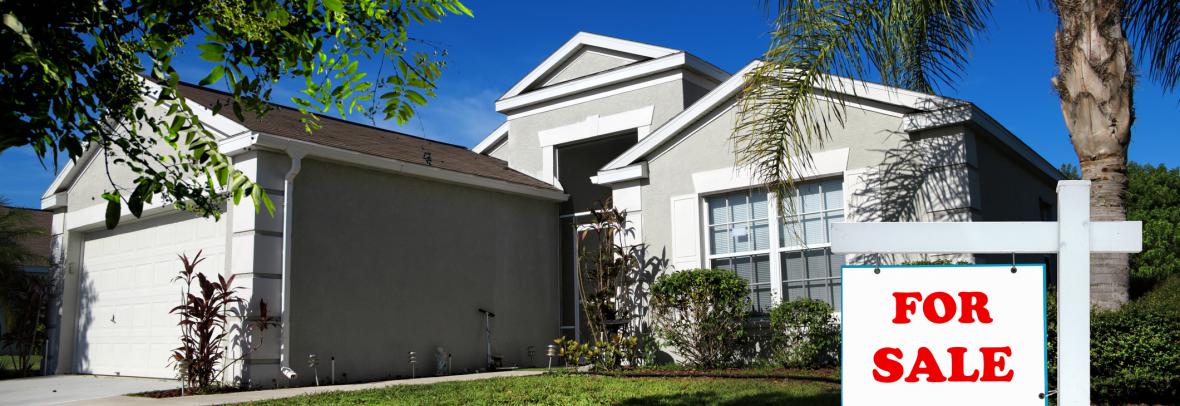 Moderate Florida home with palms trees and a for sale sign