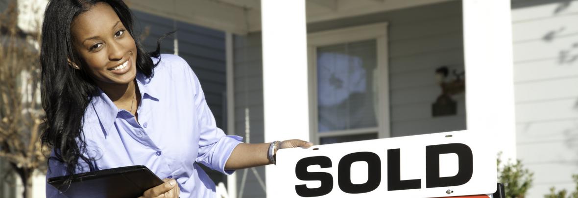 Woman smiling beside a for-sale sign with sold posted over it