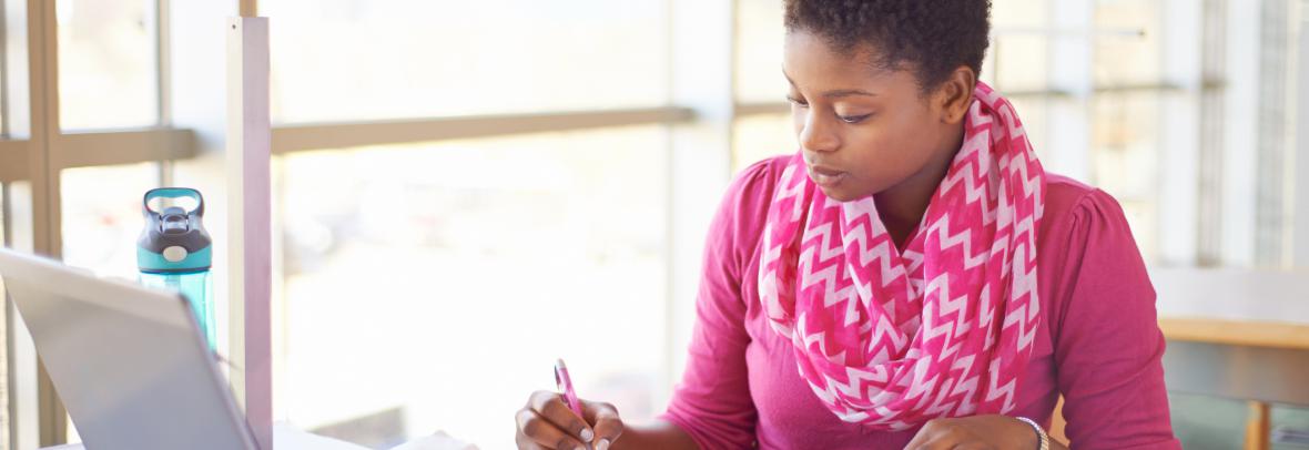 Woman writing in notebook in front of laptop