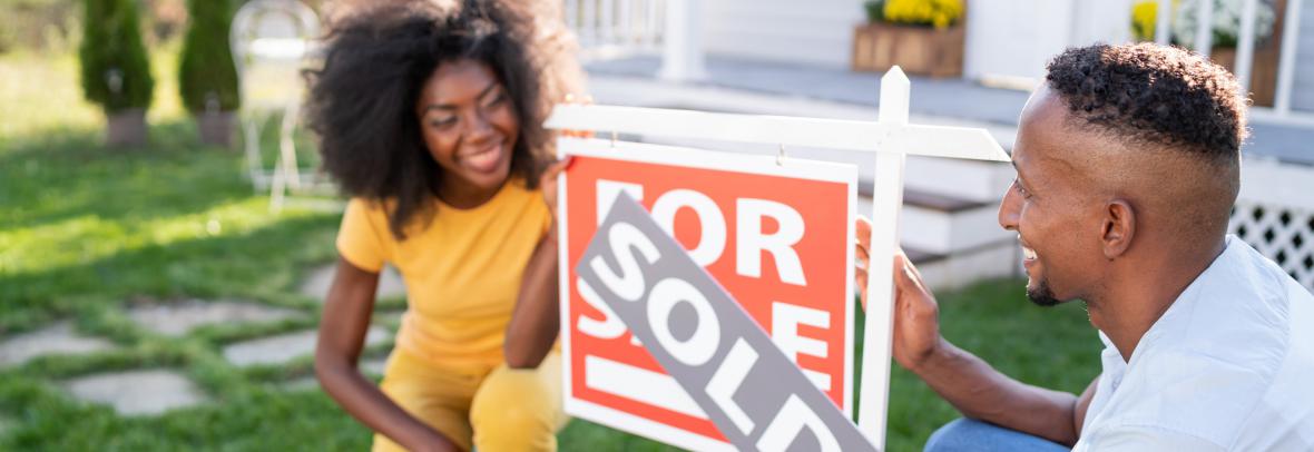 Husband and wife showing off sold sign in front of house