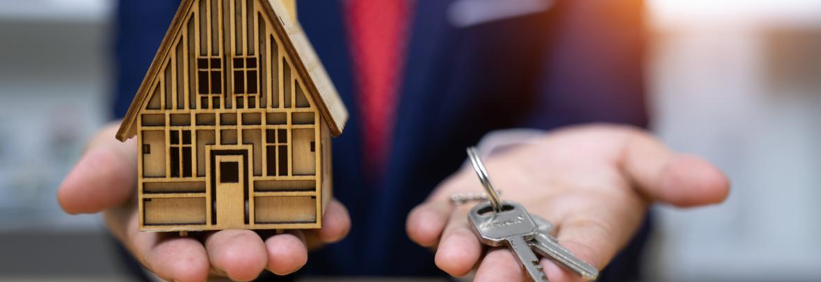 Blurry man in suit holds small house and keys in his hands