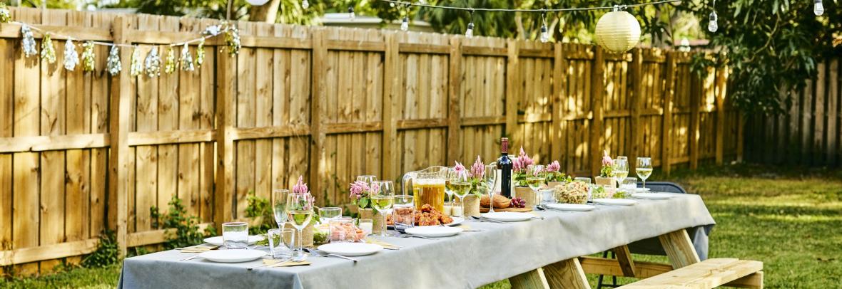 Large picnic table set for a meal in a yard with a fence