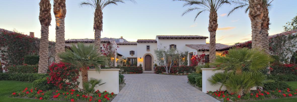 Large luxury home with landscaped entryway bordered by palm trees