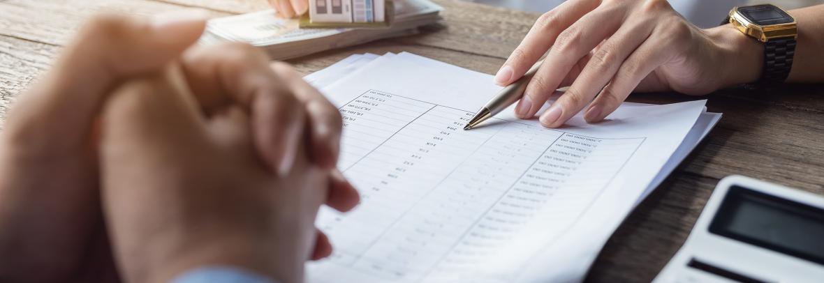 Loan agreement, real estate agent or bank officer describes the loan interest to the customer, along with loan documents with a home-style pen and a replica money on a wooden table. -