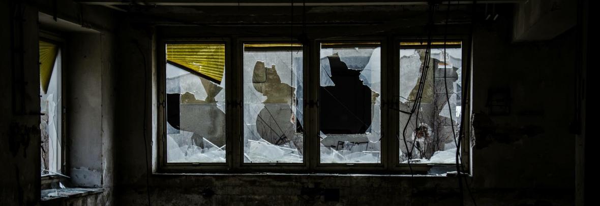 A row of broken windows and trash on the floor inside a fixer-upper