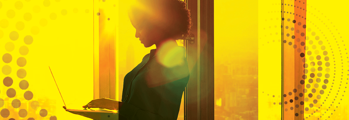 Photo of a woman standing looking at her laptop with a yellow color wash