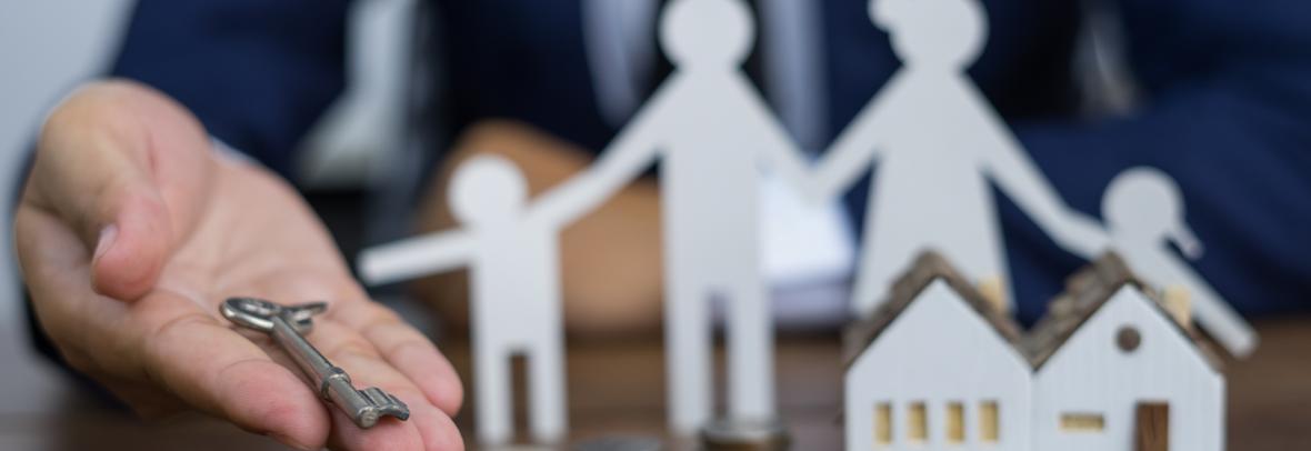 hand holding a key with family paper figures and small toy house in background