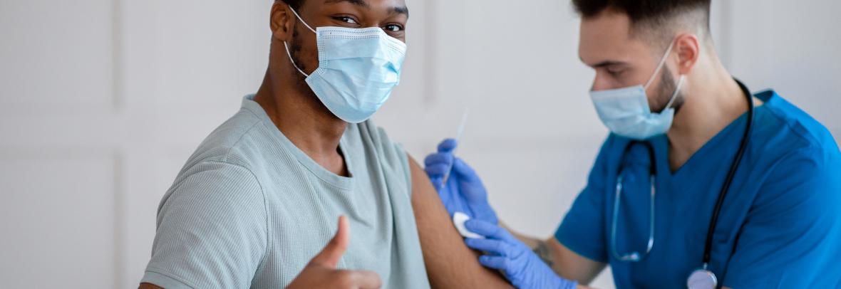 African American man in mask gesturing thumb up during coronavirus vaccination, approving of covid-19 immunization