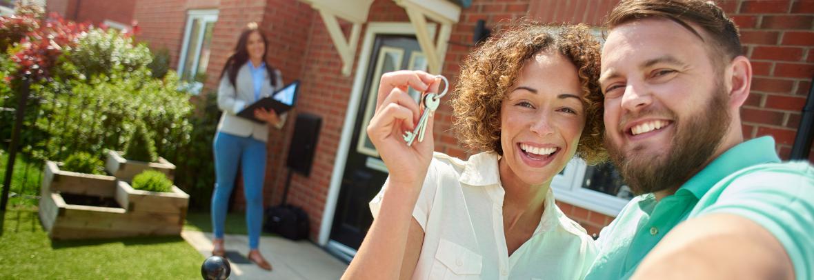 a young couple celebrate getting the keys to their new home by taking a selfie in the garden