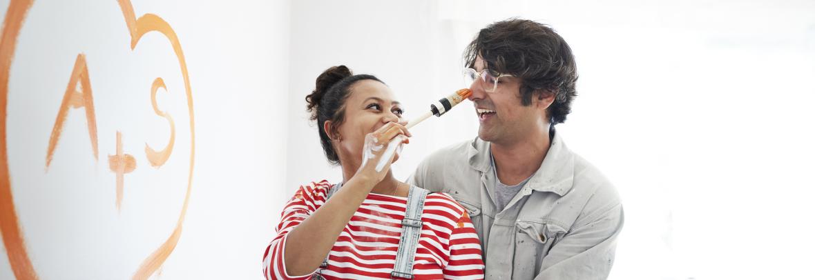 Pregnant woman painting man's nose playfully after putting heart on a wall