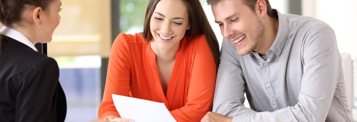 Realtor talking with a couple of happy customers sitting in a desktop at office