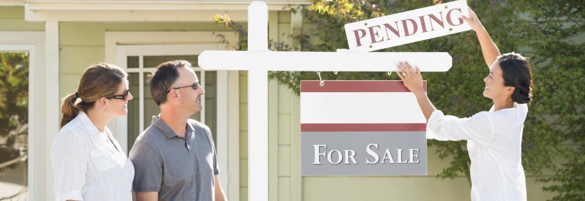 Couple watches their Realtor add a pending sign to a home's for-sale sign