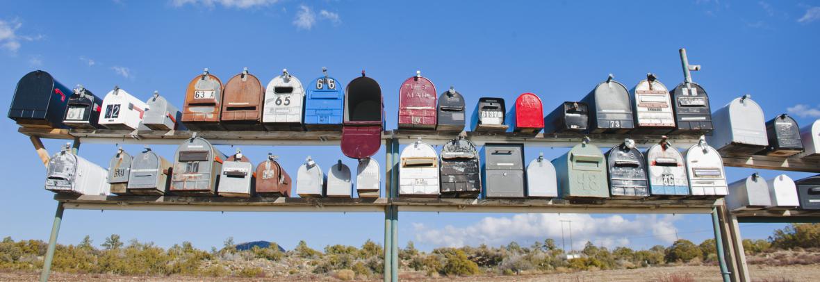 Row of country mailboxes in different colors against a deep blue sky with clouds