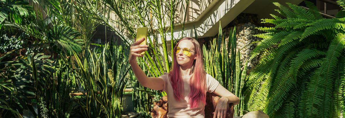 A woman taking a selfie photo amid an inside garden with trees and plants