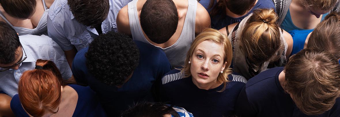 Photo of a woman looking up at the camera among man other people looking down