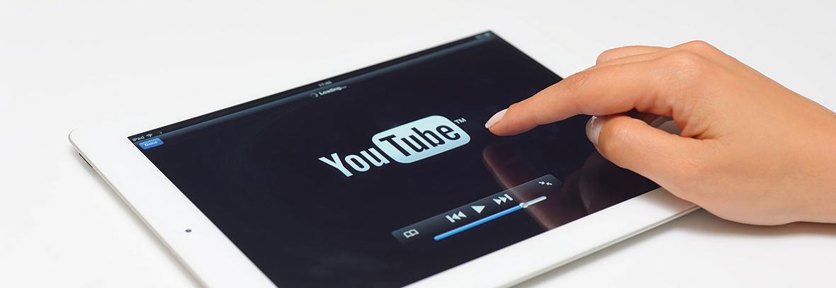 Photo of YouTube logo on an iPad with a hand pointing at it