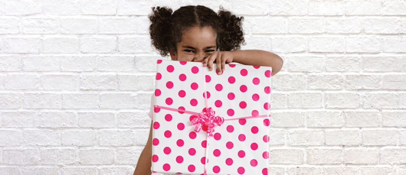 Photo of little girl holding a present wrapped in pink polka dotted wrapping paper